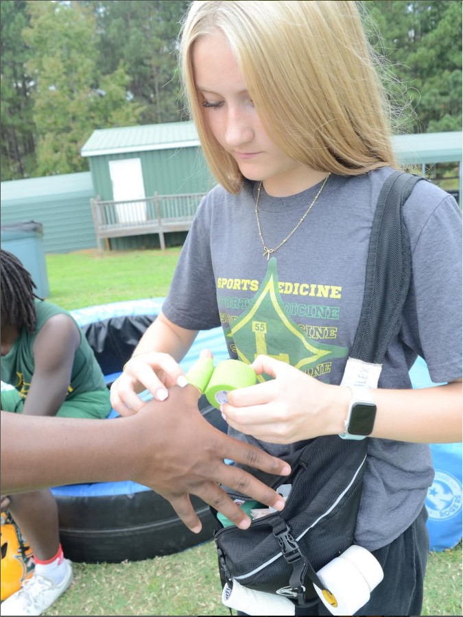 Sophomore Athletic Trainer Alex Marion bandages a football players hand during practice.